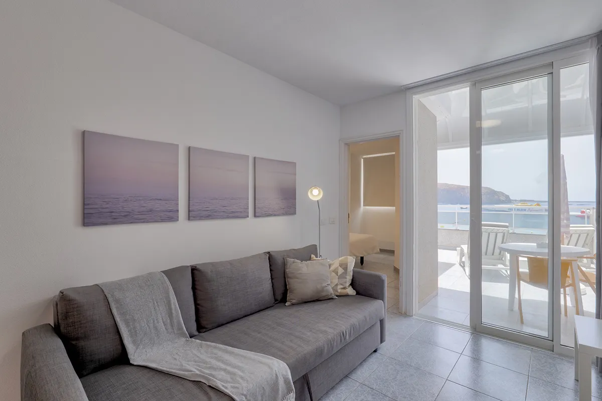 Sala con sofá gris y vista al mar por puerta corrediza de vidrio.