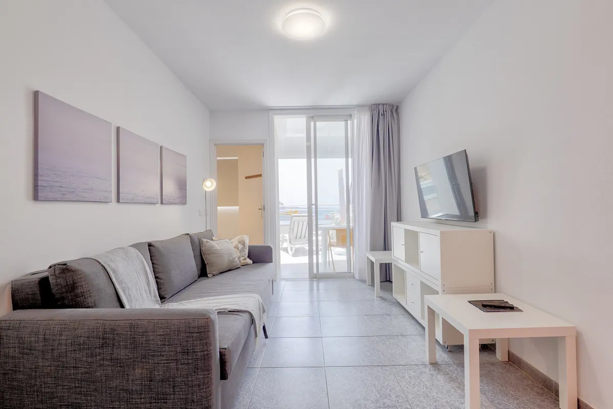 Sala moderna con sofá gris, televisor y puerta corrediza hacia un balcón.