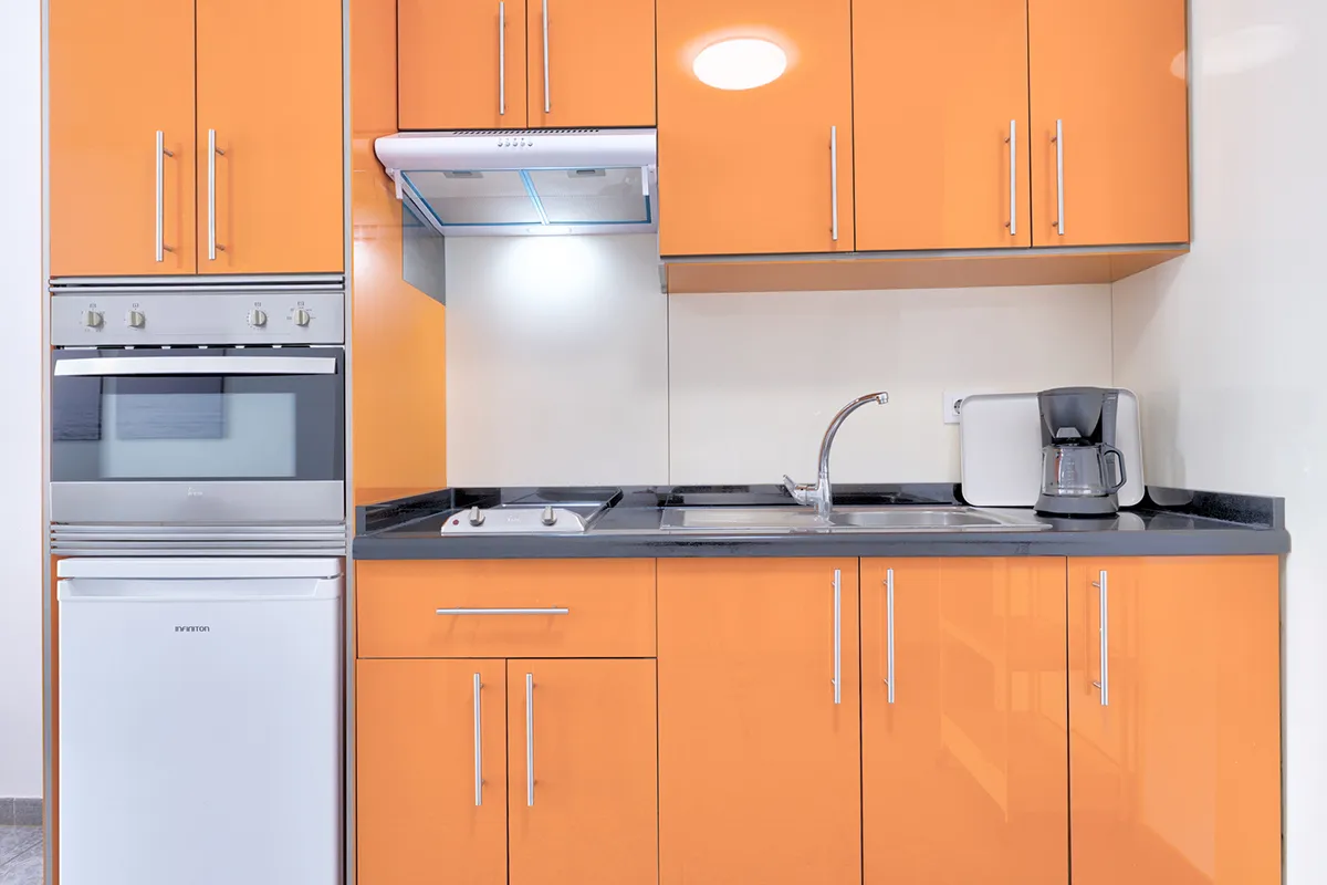 Cocina moderna con muebles naranjas y electrodomésticos de acero inoxidable.