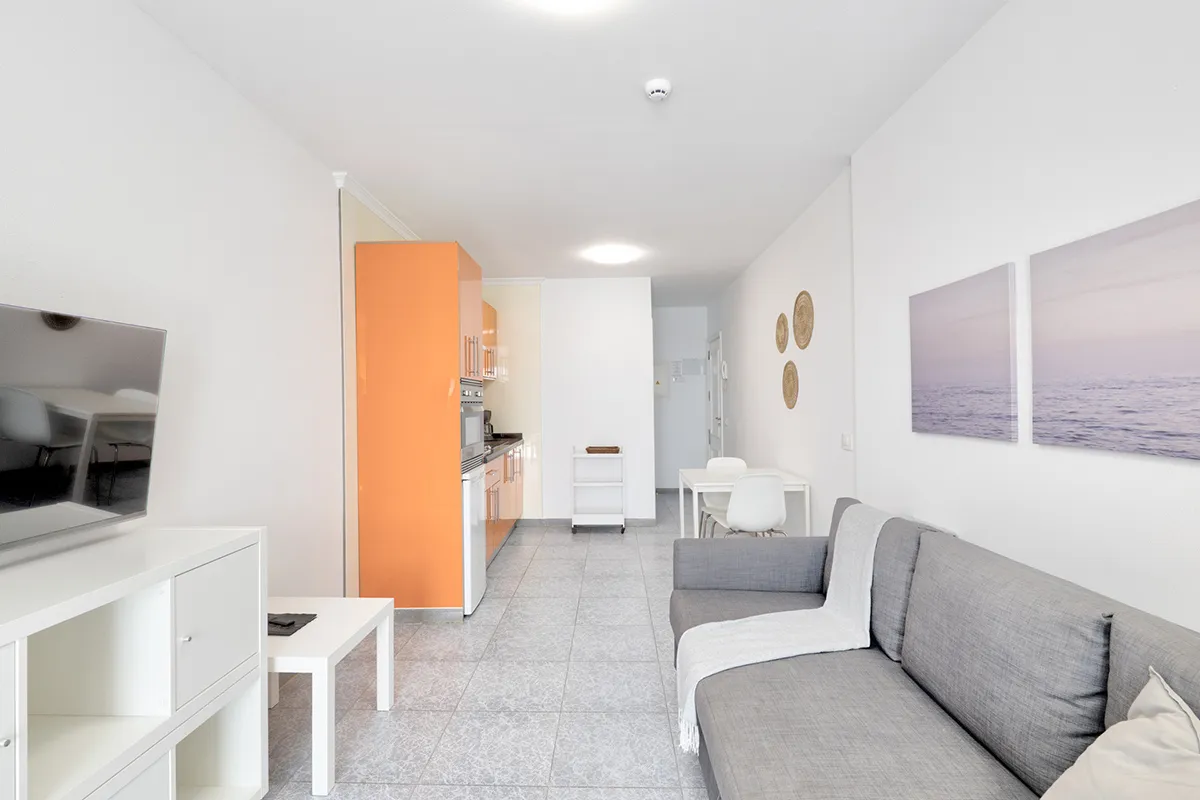 Sala moderna con sofá gris y cocina naranja al fondo.