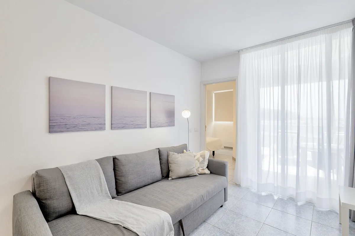 Sala moderna con sofá gris y cuadros, entrada a dormitorio al fondo.