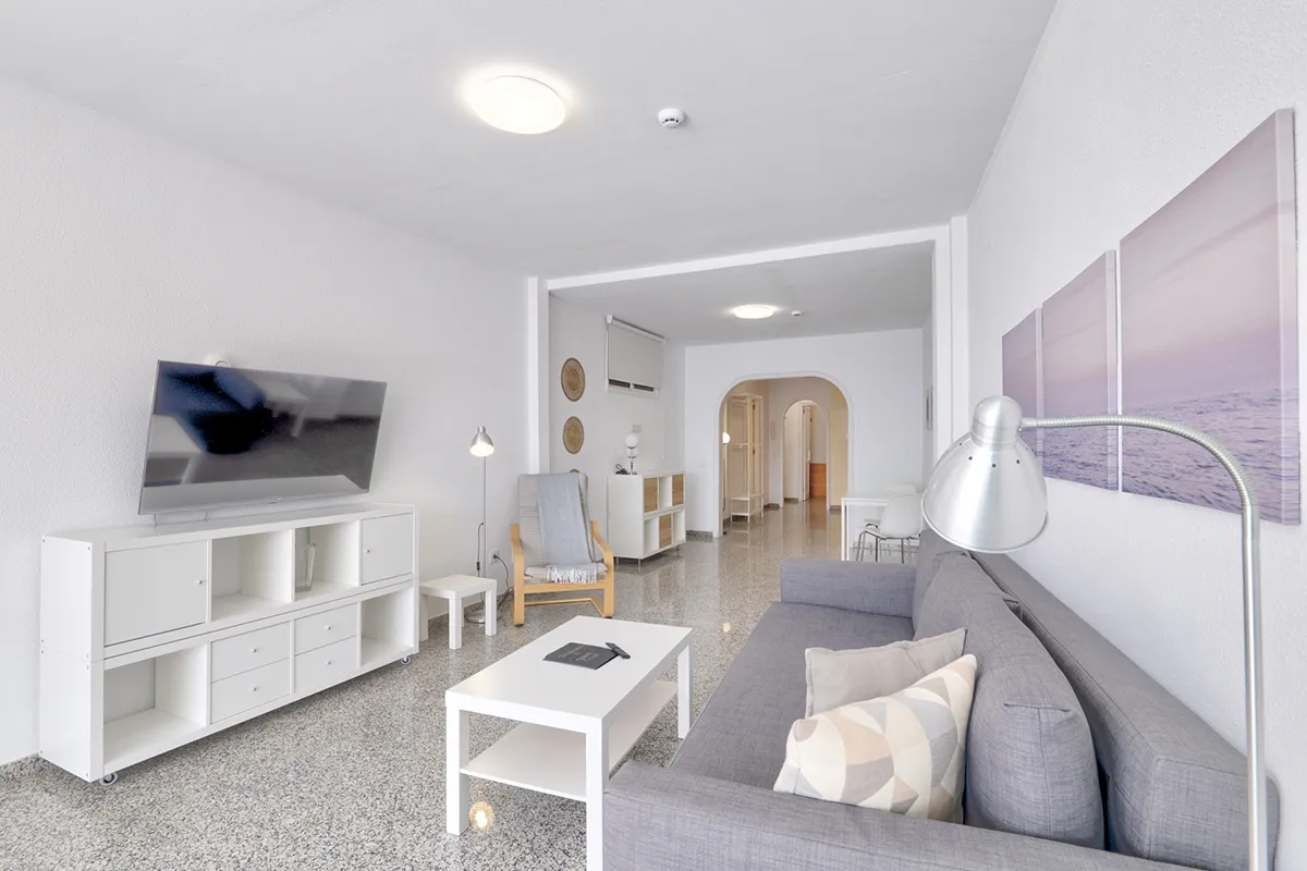 Sala moderna con sofá gris, televisor y decoración sencilla y luminosa.