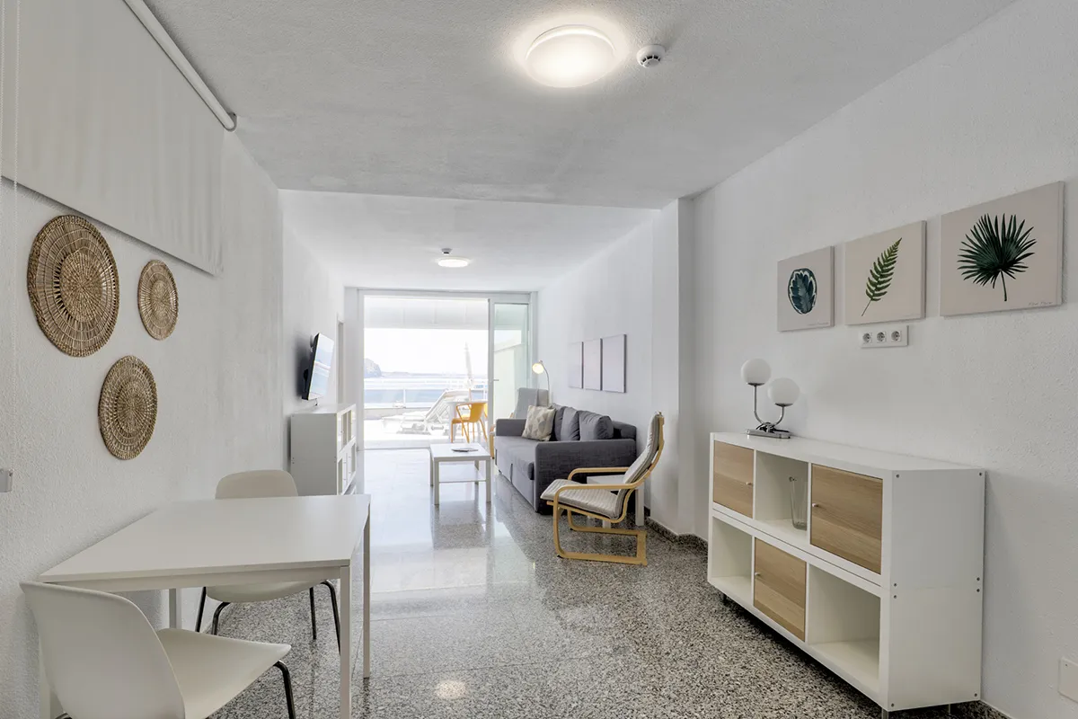 Sala moderna y luminosa, decorada en blanco con vista al mar y balcón.