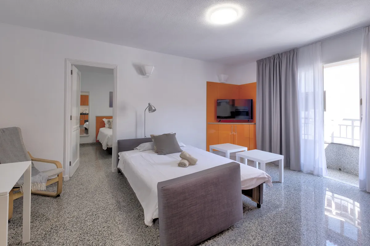 Habitación moderna con cama, televisor y balcón iluminado.