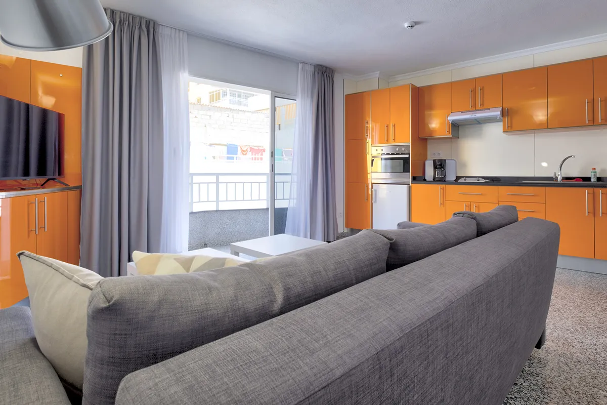 Sala moderna con cocina naranja y sofá gris junto a una ventana grande.