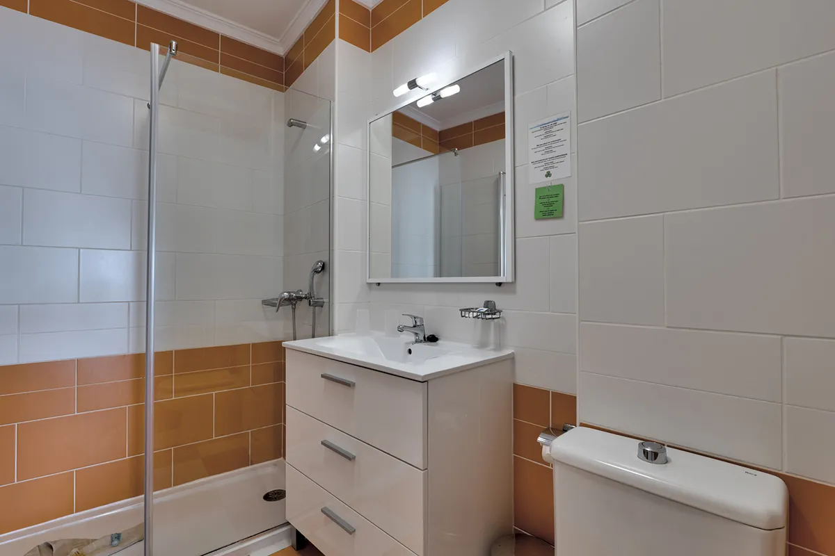 Baño moderno con azulejos naranjas y blancos, espejo y lavabo.