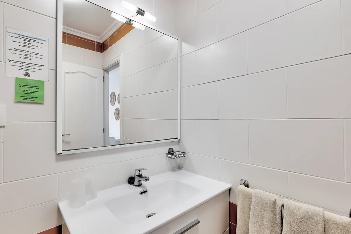 Baño pequeño con espejo grande, lavamanos y toallas colgadas en la pared.