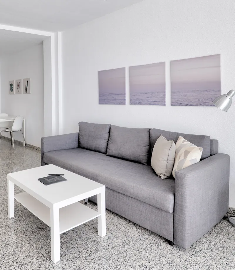 Sala moderna con sof&aacute; gris, mesita blanca y cuadros en la pared.