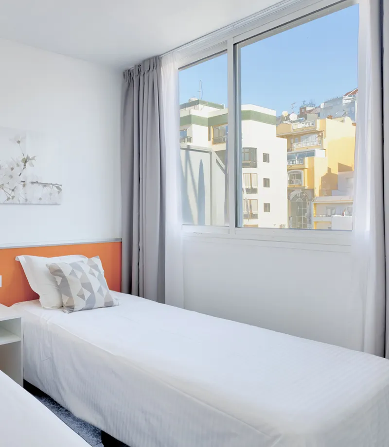 Cuarto luminoso con dos camas individuales y gran ventana.