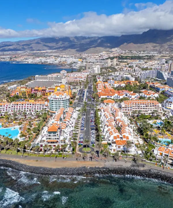 Vista a&eacute;rea de una ciudad costera con edificios y monta&ntilde;as al fondo.