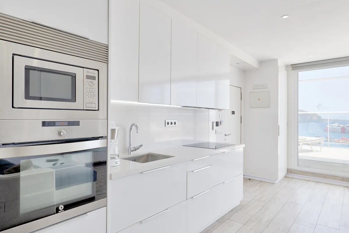 Cocina moderna blanca con electrodomésticos y vista al mar.