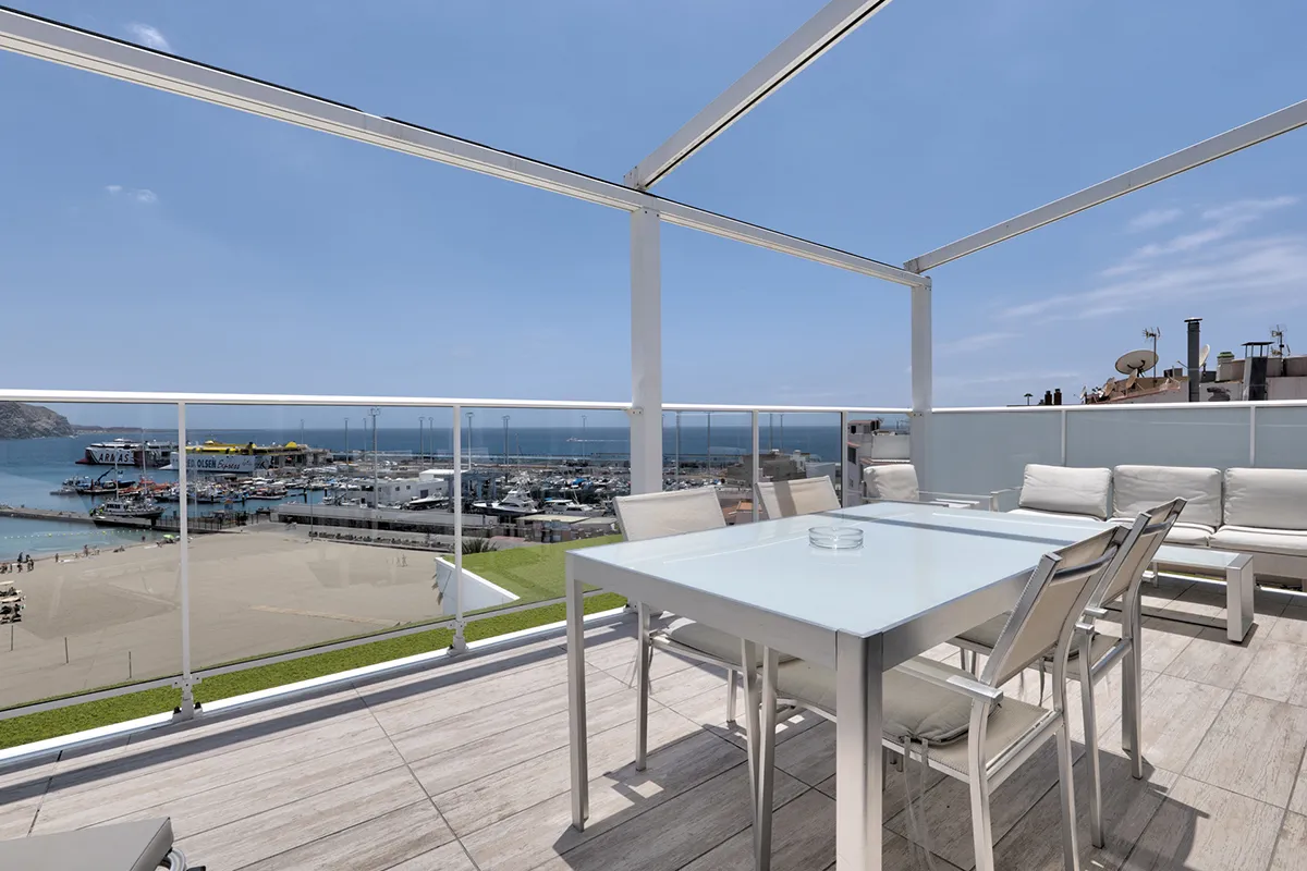 Terraza con comedor exterior y vista al puerto y mar azul bajo un cielo despejado.