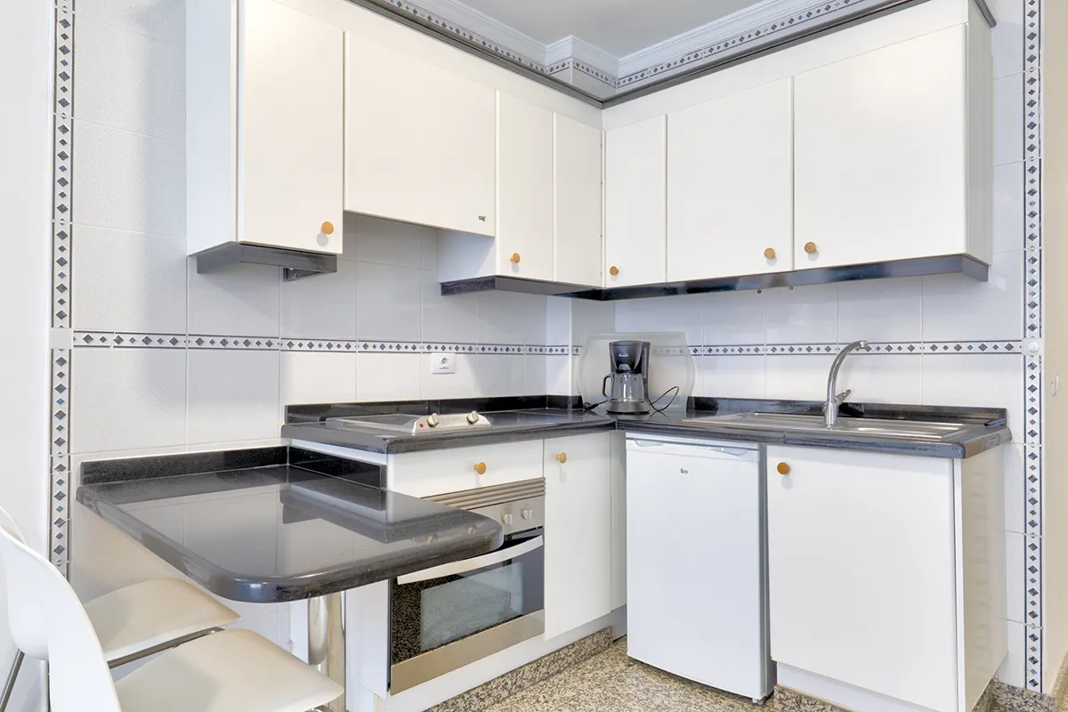 Cocina blanca con electrodomésticos y encimera negra.