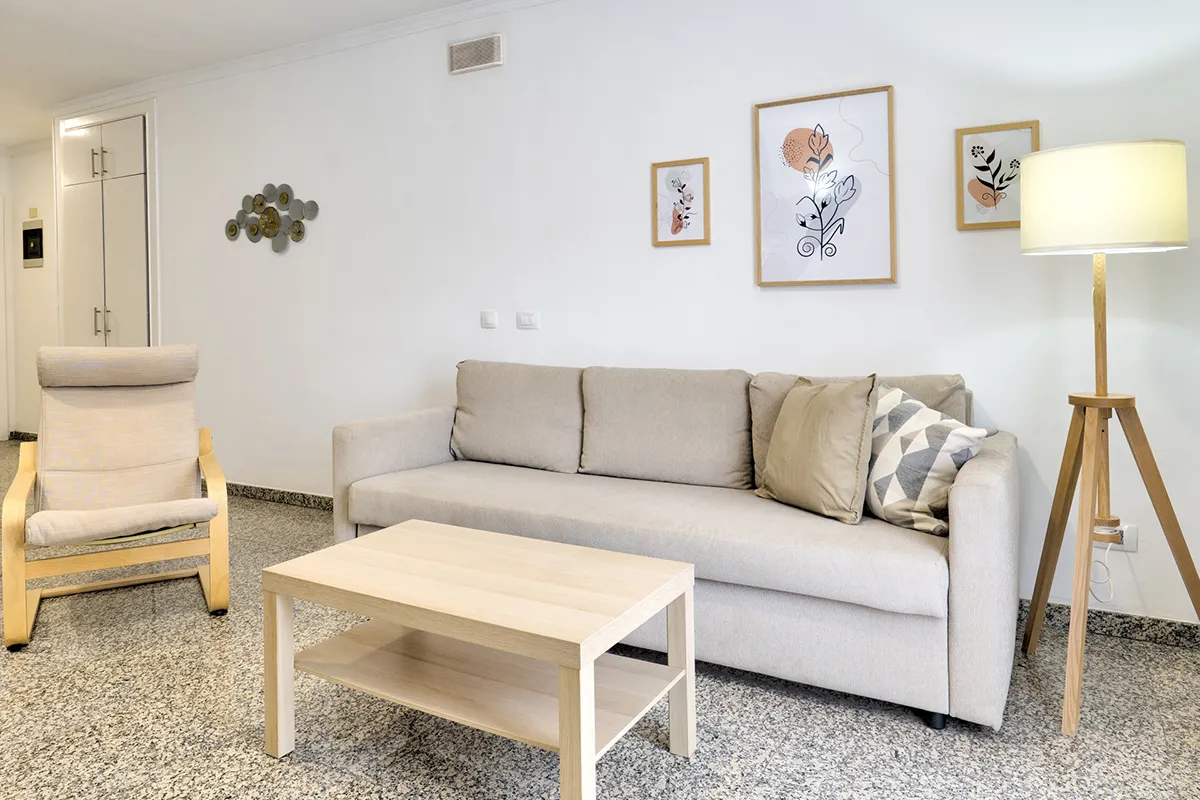 Sala moderna con sofá beige, silla, mesa de madera y lámpara de pie.