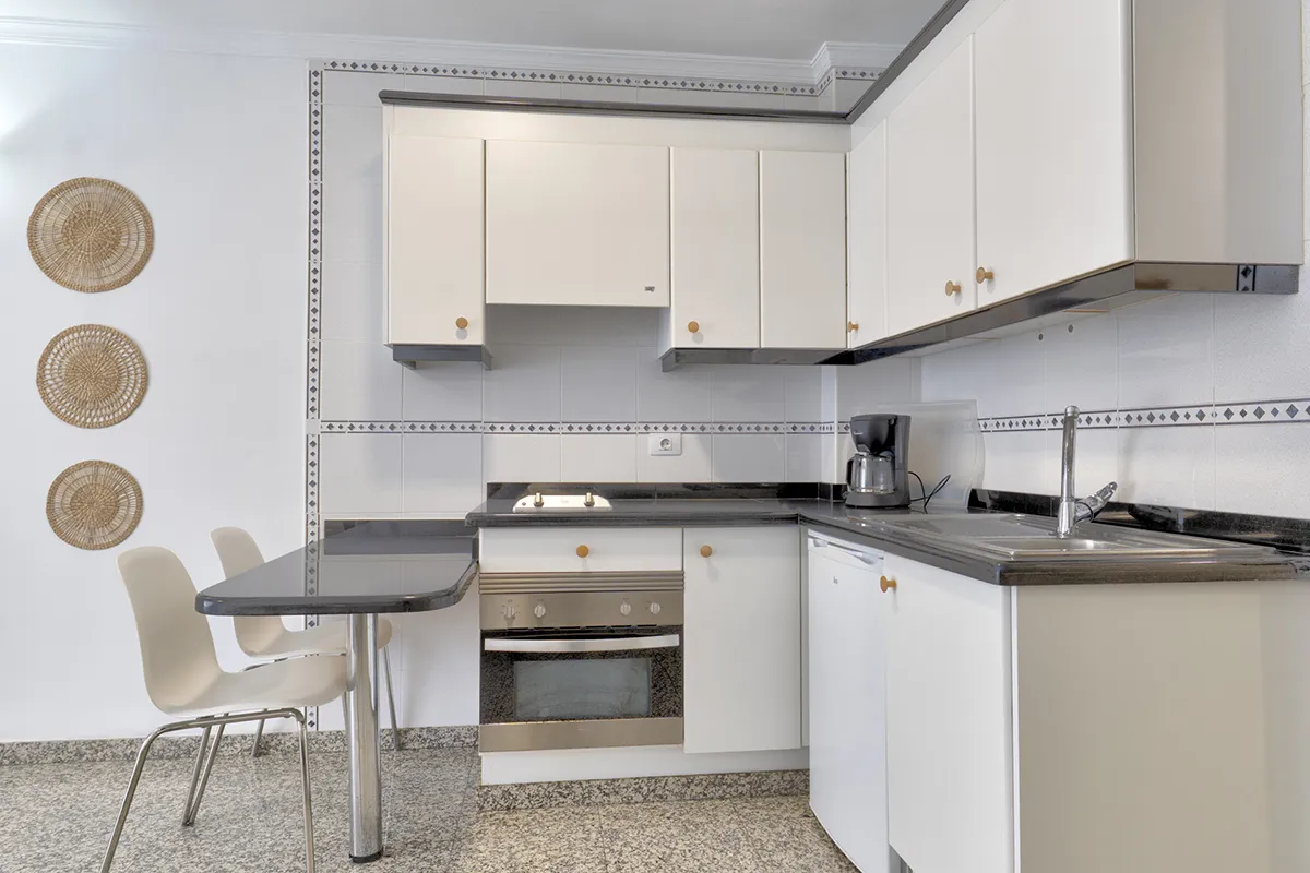 Cocina blanca con encimeras negras, horno, cafetera y decoración en la pared.