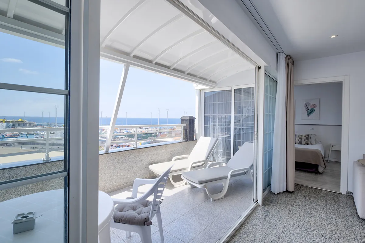 Terraza con vista al mar, tumbonas y mesa con sillas blancas. Habitación al fondo.