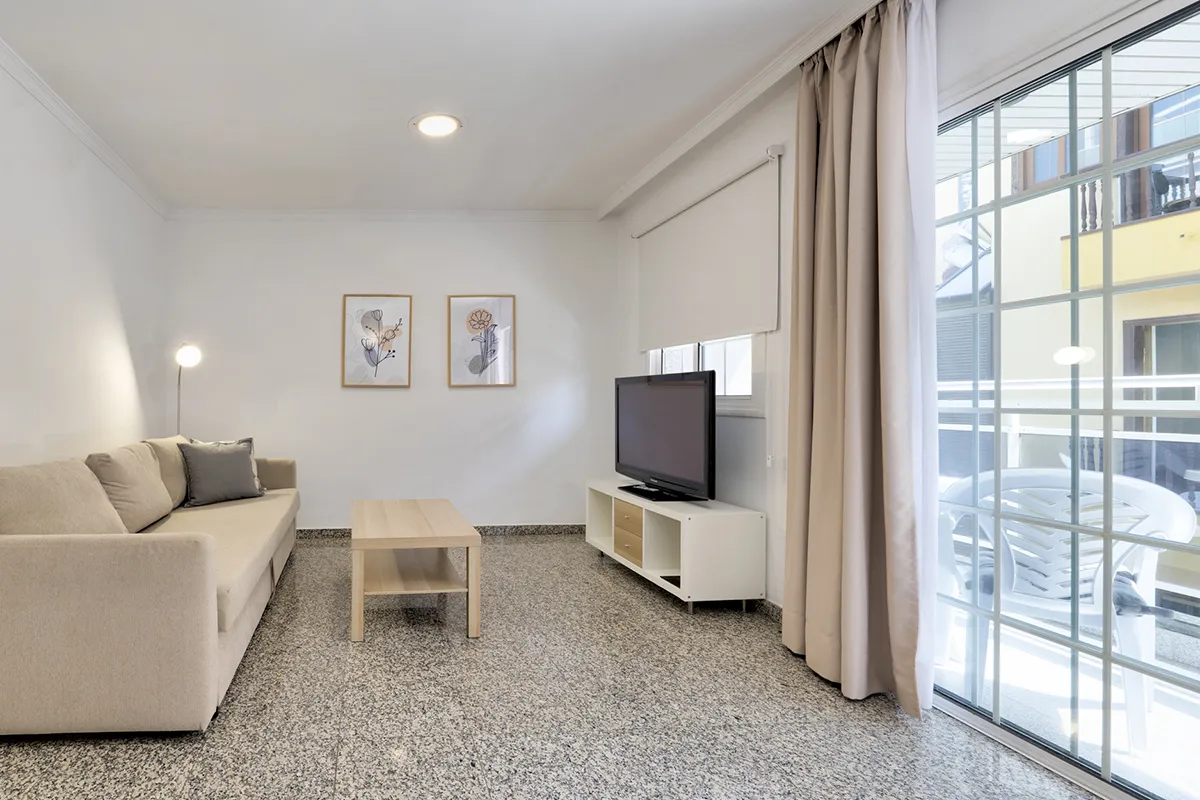 Sala de estar moderna con sofá beige y televisor junto a ventanal.