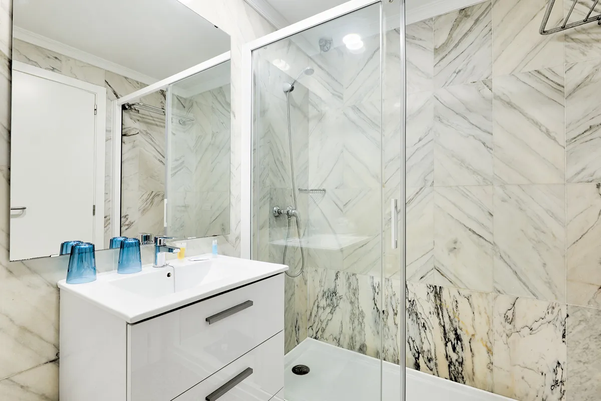 Baño moderno con azulejos claros y ducha de cristal.