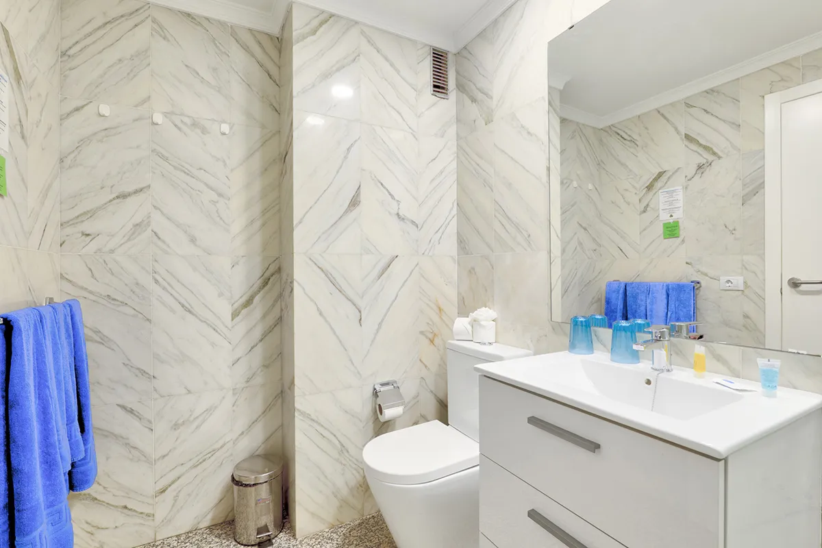 Baño moderno con paredes de mármol y toallas azules.