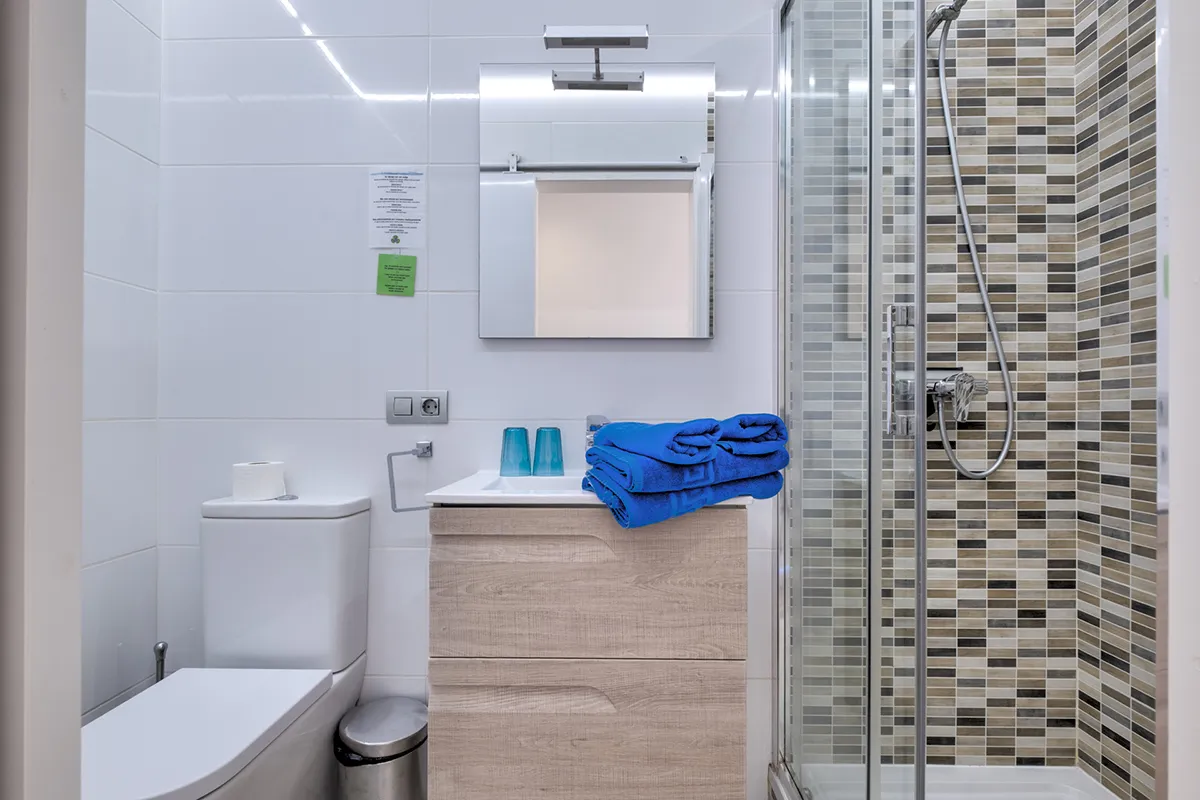 Baño moderno con ducha, espejo, lavabo, toallas y azulejos.