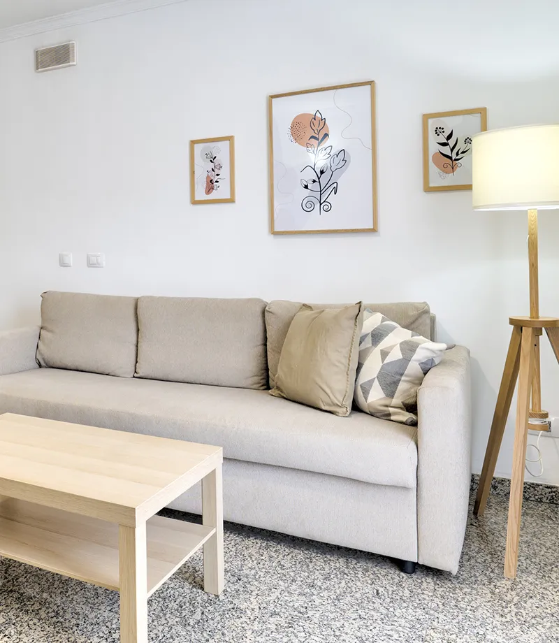 Sala moderna con sof&aacute; beige, mesa de madera y l&aacute;mpara junto a cuadros decorativos.