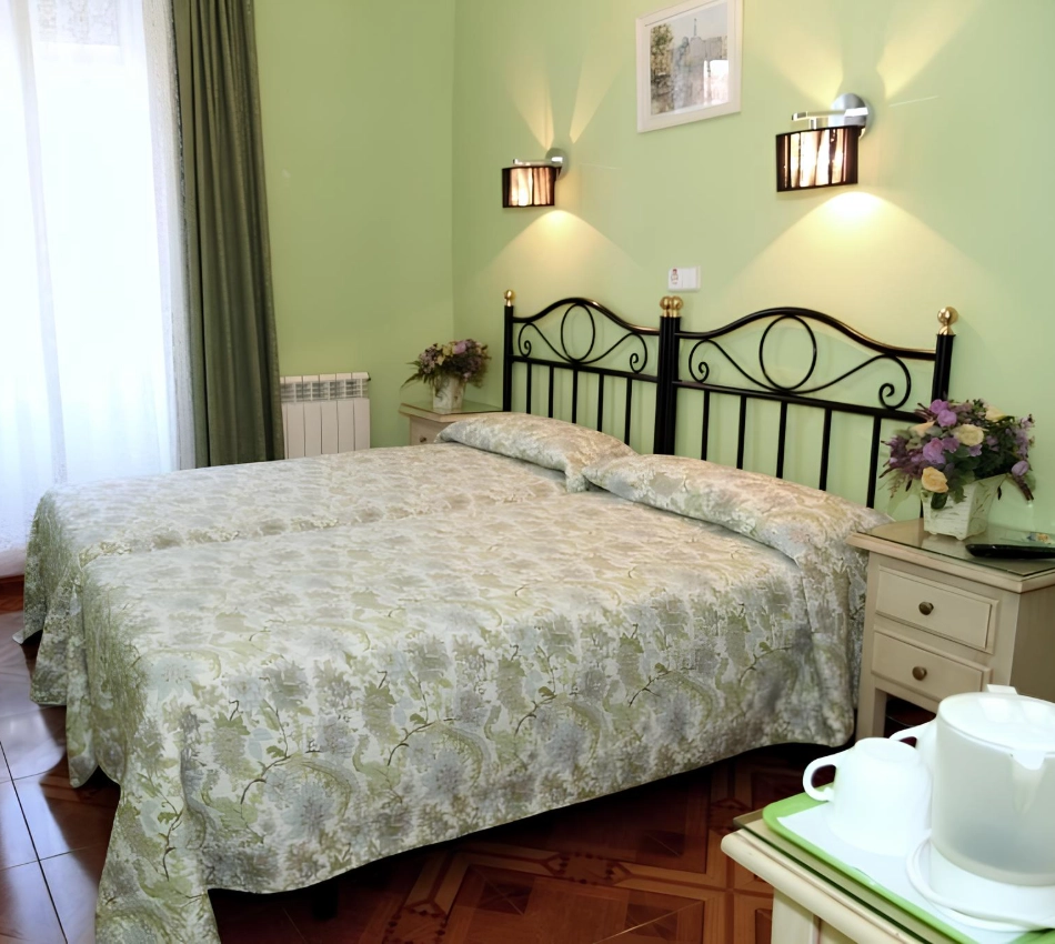 Habitaci&oacute;n con dos camas individuales, paredes verdes y decoraci&oacute;n floral.