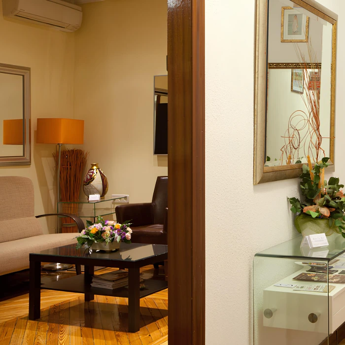 Sala de espera elegante con sof&aacute;s, mesa de vidrio, flores y decoraci&oacute;n moderna.