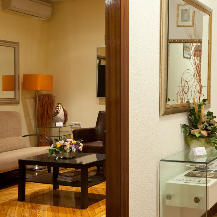 Sala de espera elegante con sill&oacute;n, mesa de cristal, espejo y decoraciones florales.