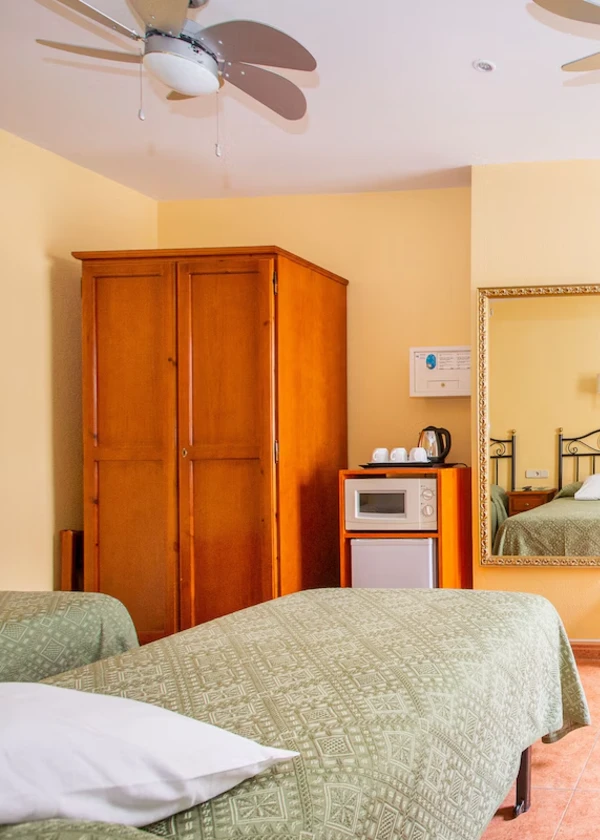 Habitaci&oacute;n con camas, armario, microondas, espejo y ventilador de techo.