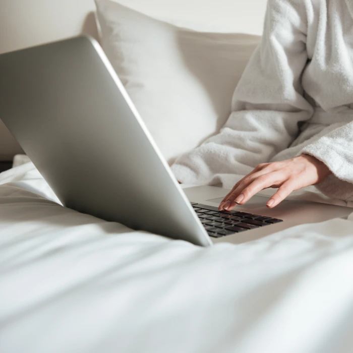 Persona en bata usando una laptop sobre la cama.
