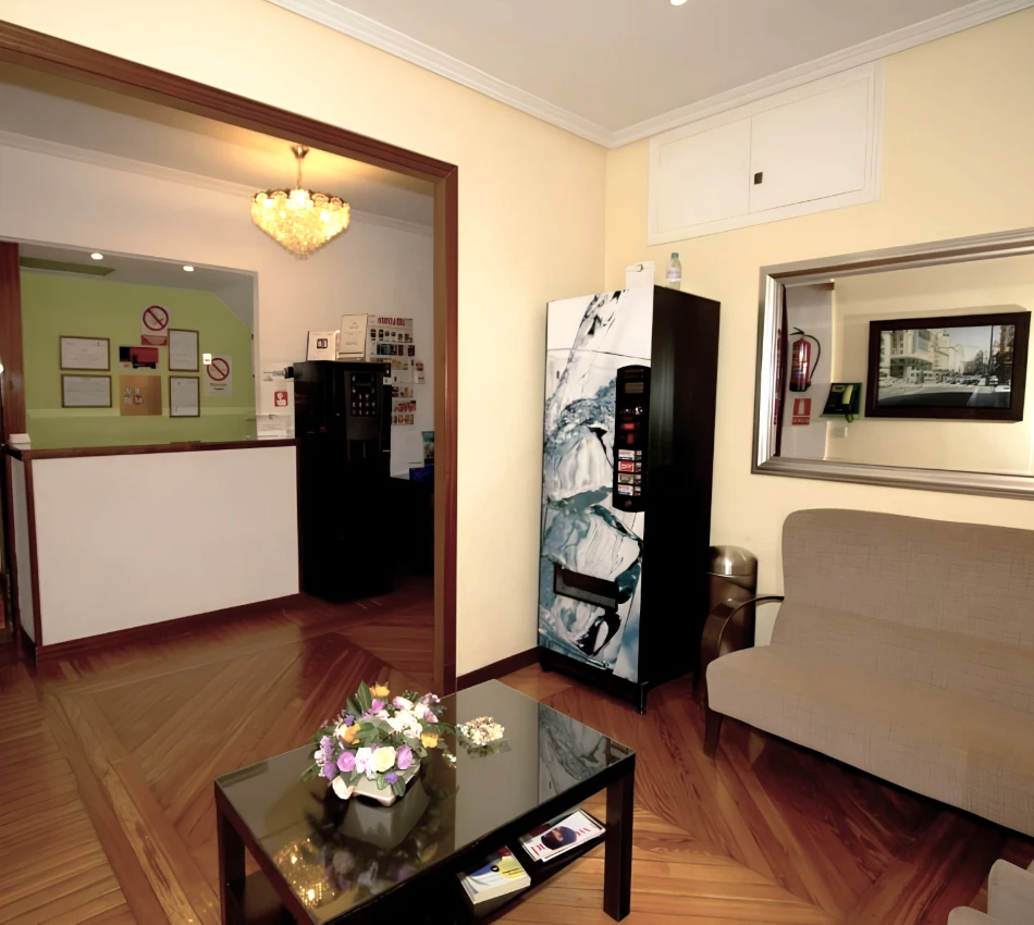 Sala de espera con sof&aacute;, m&aacute;quina expendedora y mesa con flores. Decoraci&oacute;n sencilla y acogedora.