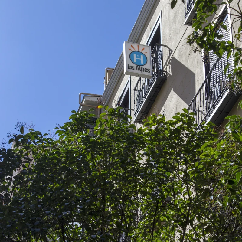 Edificio con letrero de "Los Alpes", junto a vegetaci&oacute;n y cielo despejado.
