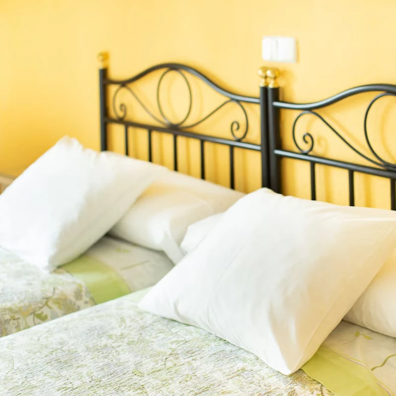 Cama con cabecero de hierro negro y almohadas blancas en habitaci&oacute;n amarilla.