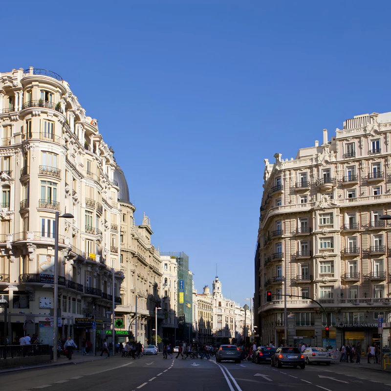 Calle de ciudad con edificios hist&oacute;ricos y tr&aacute;fico bajo un cielo despejado.
