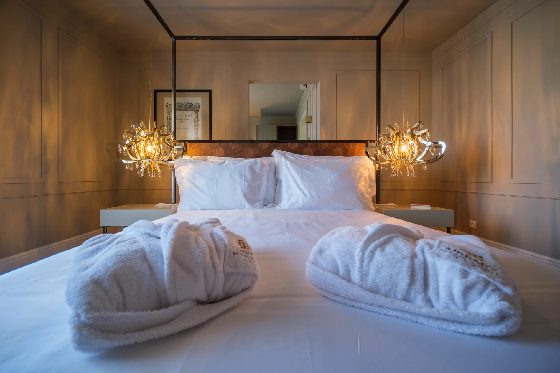 Cama de casal elegante com abajures de cristal e roup&otilde;es brancos.