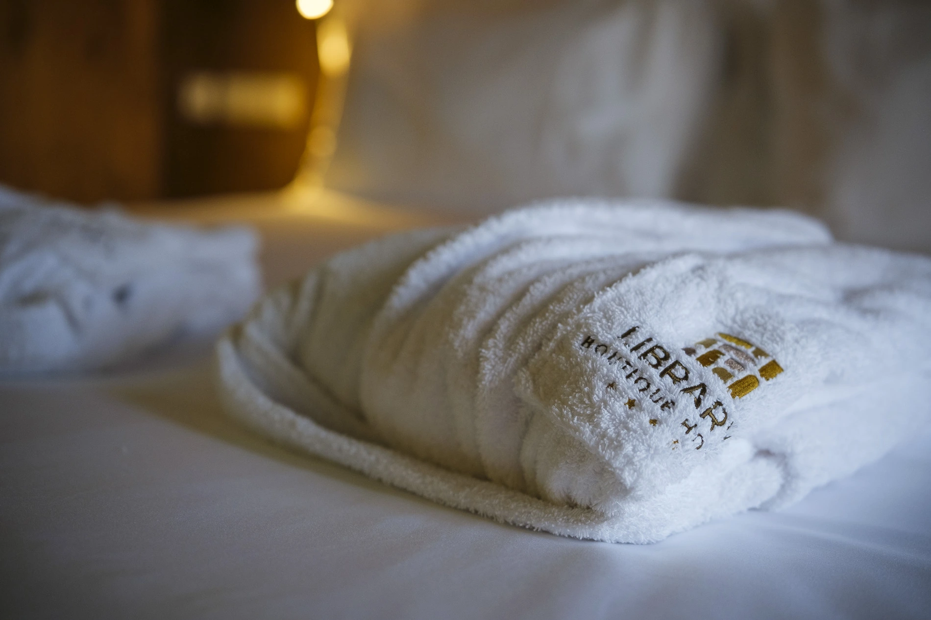 Roup&atilde;o de hotel branco com bordado em cima da cama.