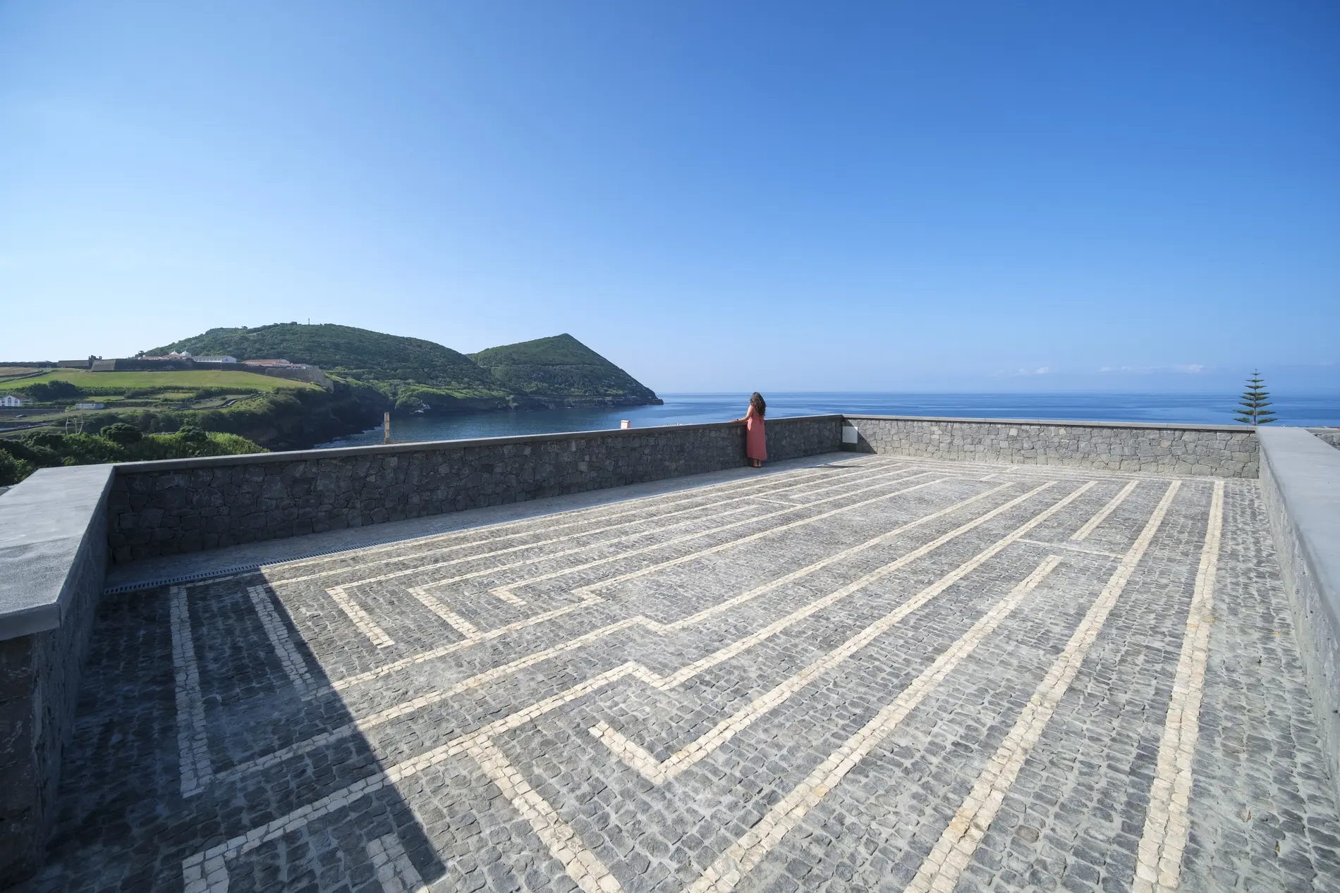 Mulher de frente para o mar em um terra&ccedil;o de pedras.