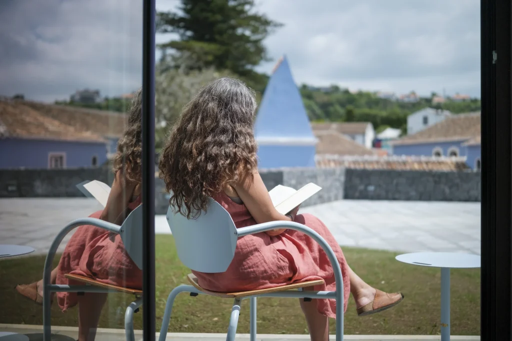 Mulher lendo ao ar livre, refletida em parede de vidro.