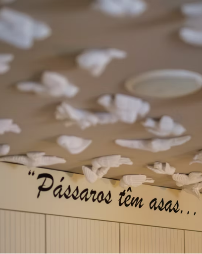 Teto decorado com esculturas de p&aacute;ssaros e frase "P&aacute;ssaros t&ecirc;m asas...".