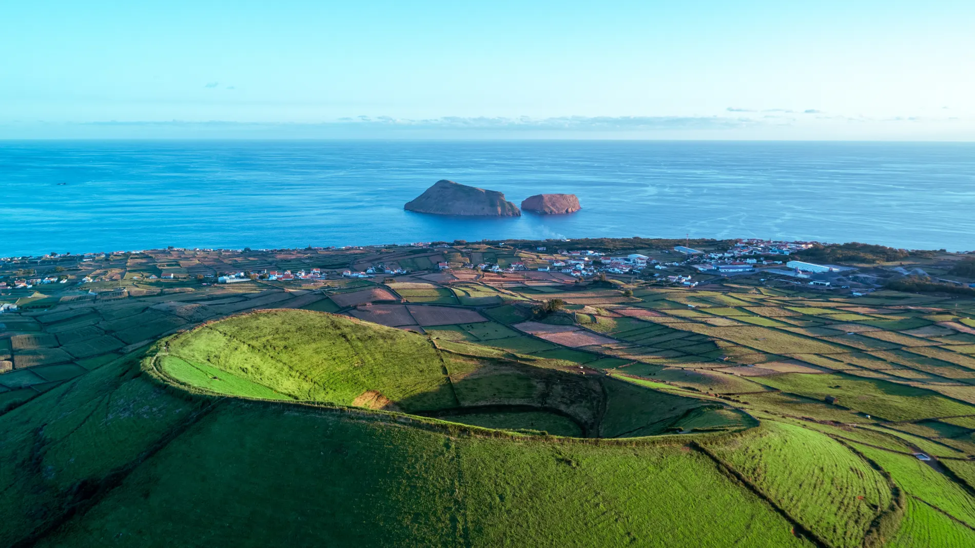 Paisagem litor&acirc;nea com campos verdes e ilhas ao fundo.