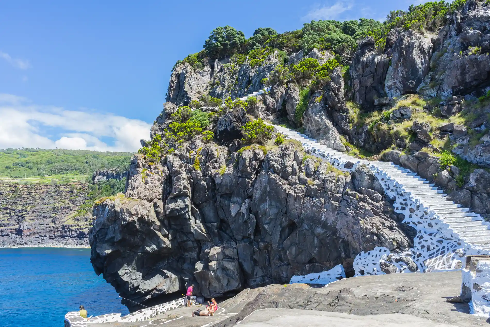 Escadaria branca em penhasco rochoso com vegeta&ccedil;&atilde;o ao lado do mar.