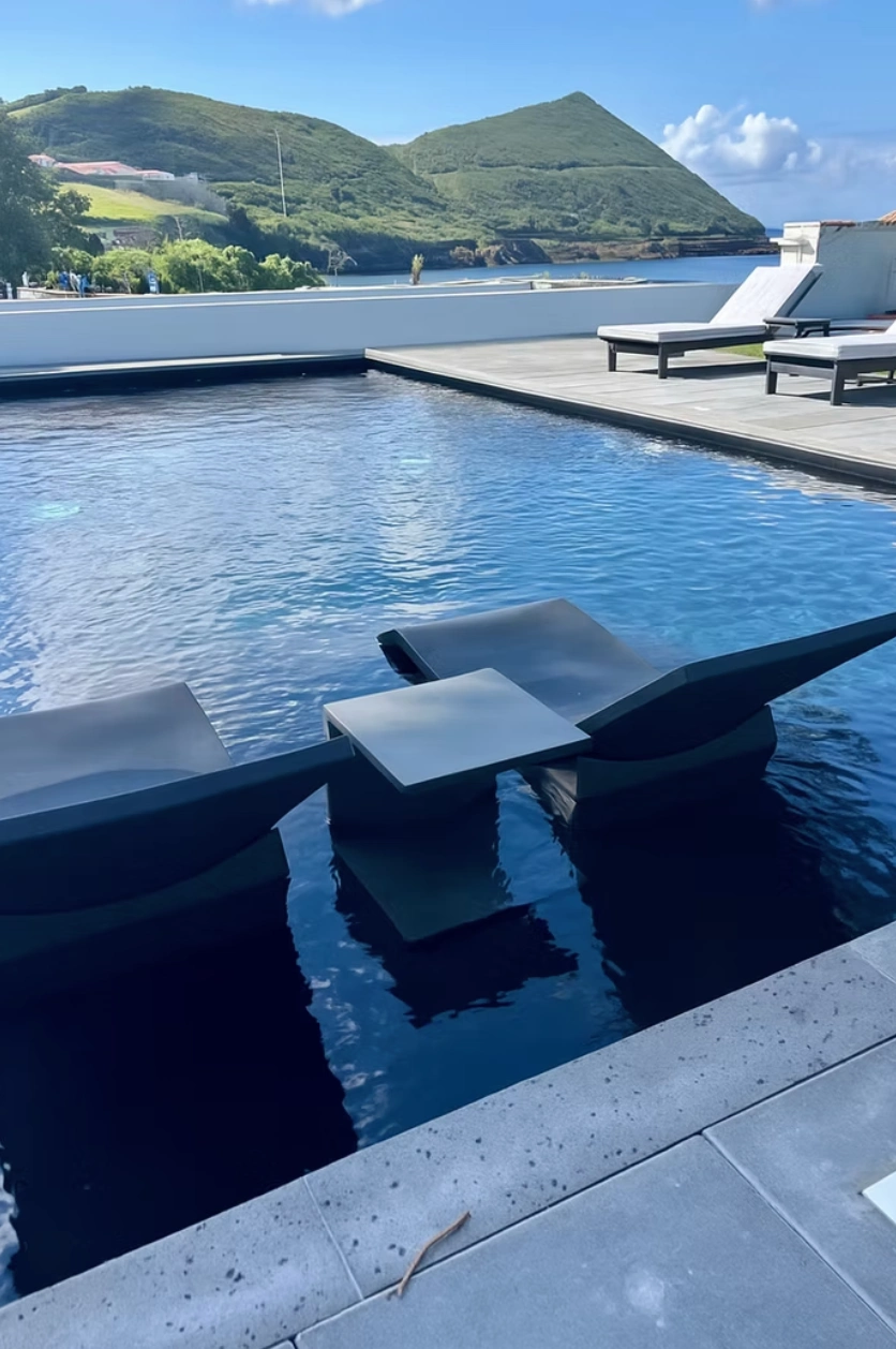 "Piscina moderna com cadeiras, vista para colinas verdes ao fundo."