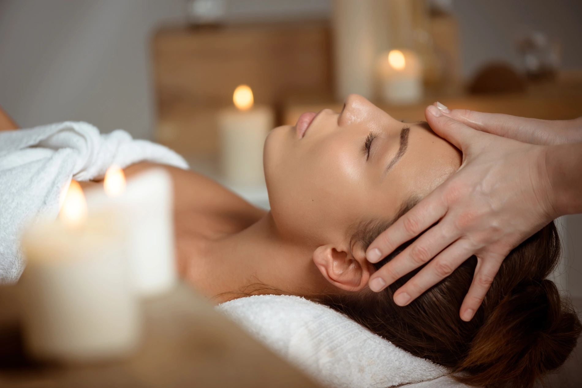 Mulher relaxa recebendo massagem facial em ambiente com velas.