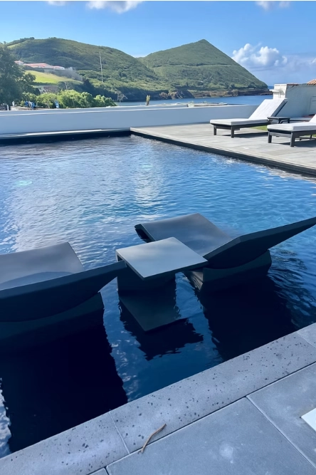 Piscina moderna com espregui&ccedil;adeiras, montanhas ao fundo.