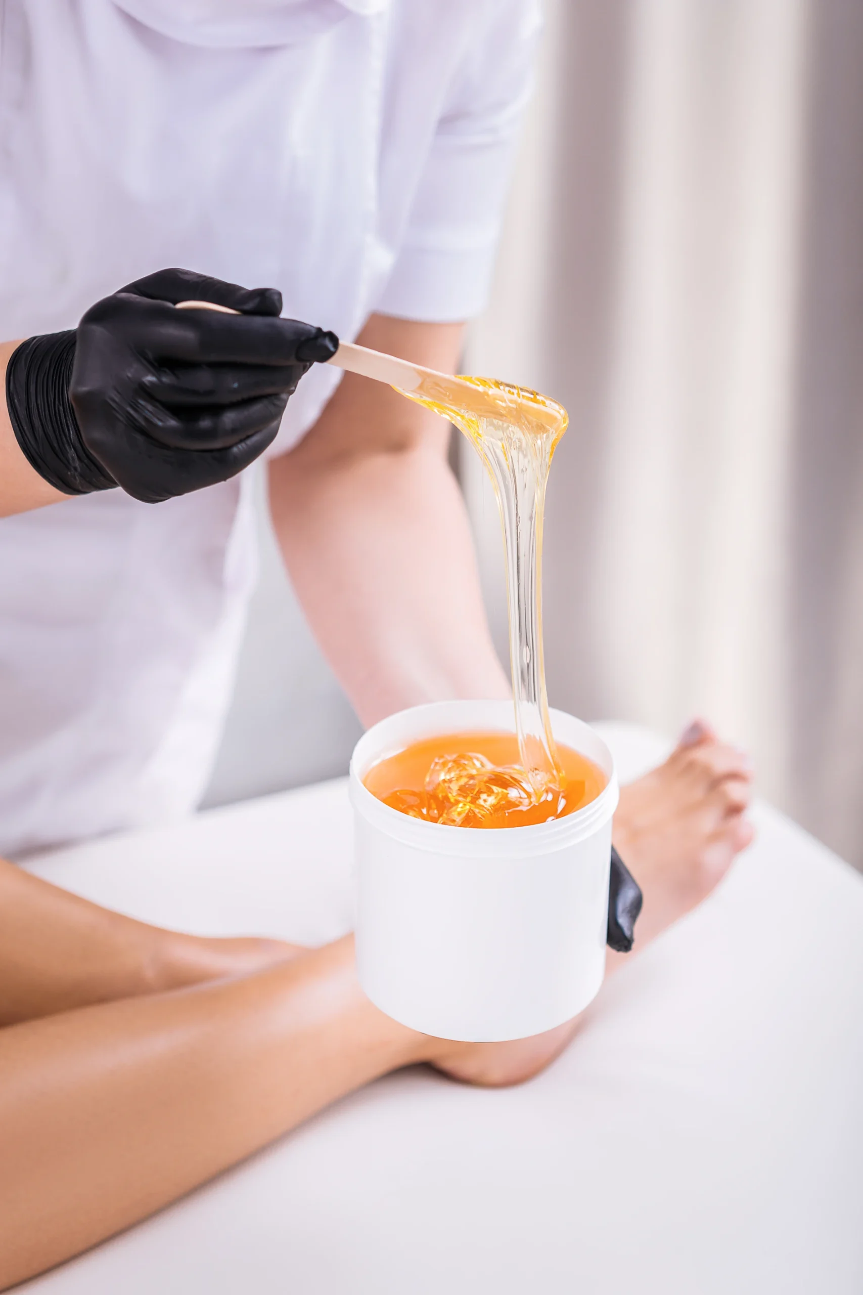 Esteticista aplicando cera com esp&aacute;tula em local de depila&ccedil;&atilde;o.