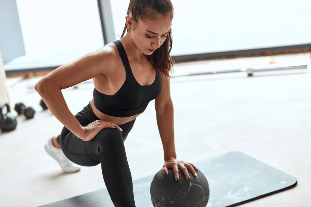 Mulher em roupa de gin&aacute;stica exercita-se com bola medicinal.