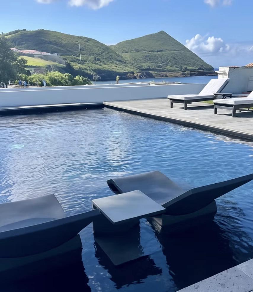 Piscina com espregui&ccedil;adeiras e montanhas ao fundo, dia ensolarado.