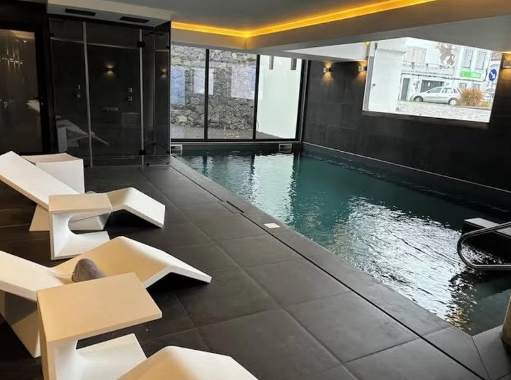 Piscina interna com design moderno e cadeiras brancas ao redor.