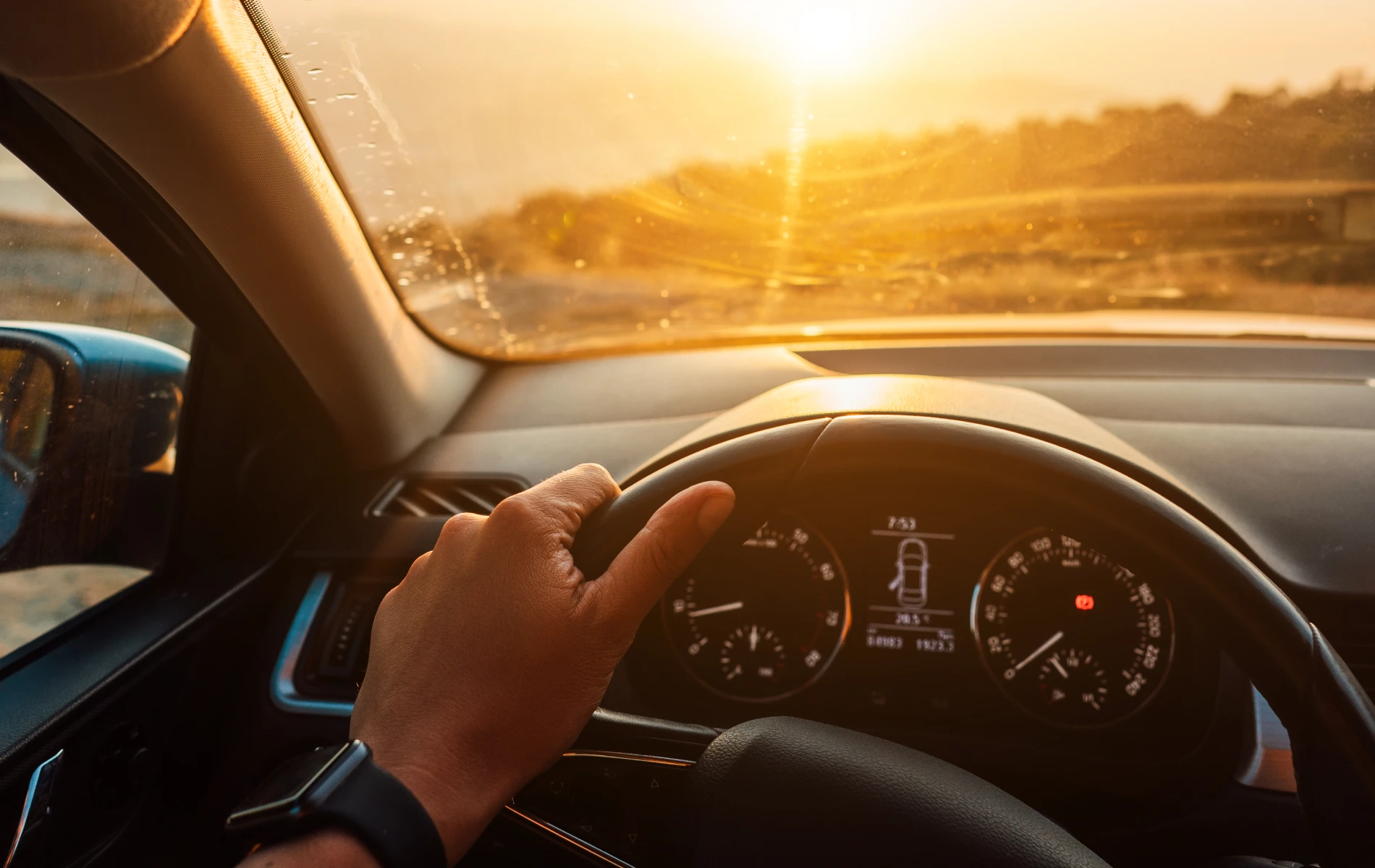 M&atilde;o no volante de carro ao entardecer, com luz solar entrando pela janela.