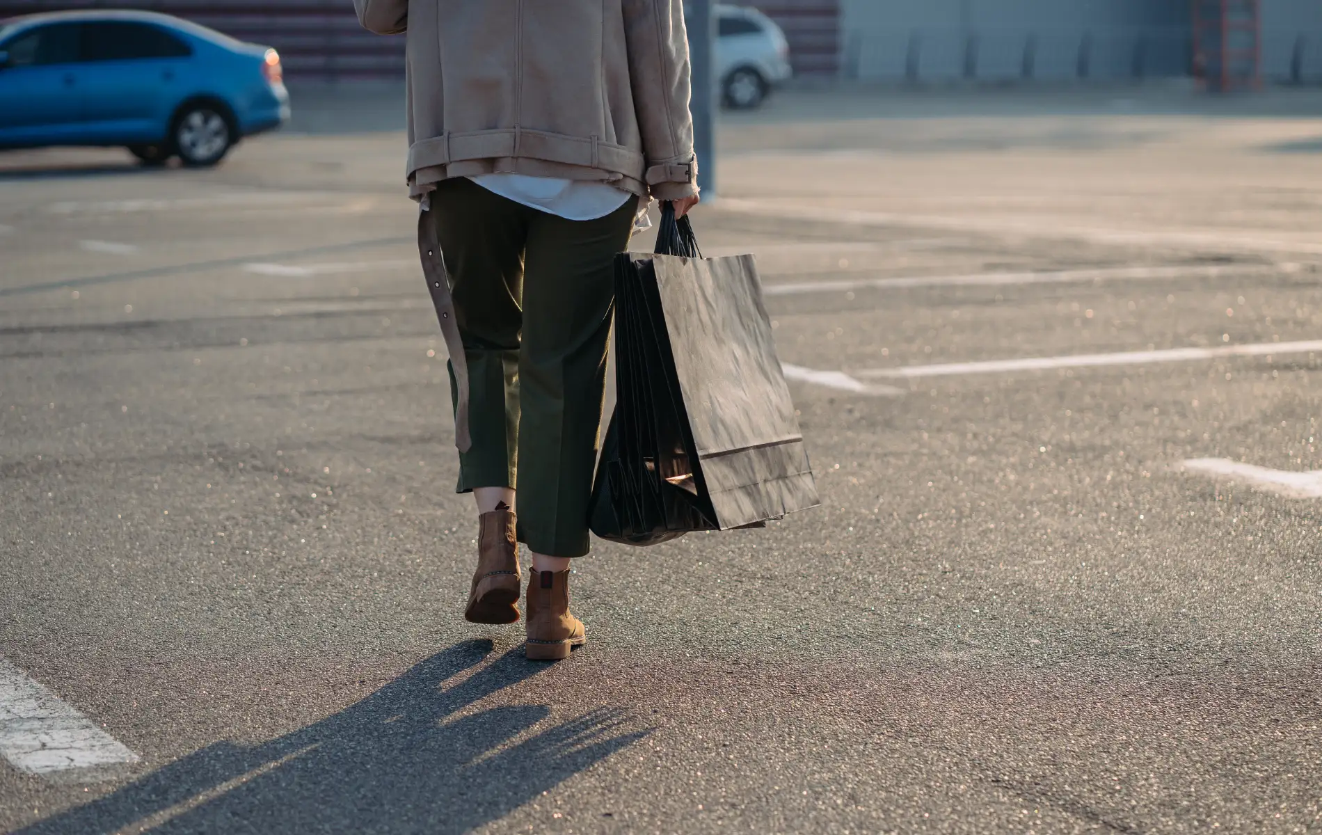 Pessoa caminhando com sacola preta em estacionamento.